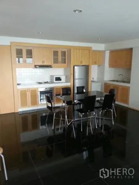 公寓 出租在Bang Rak, Bangkok - 整体厨房，木质柜体、灶台、冰箱，中间摆放黑色餐桌。