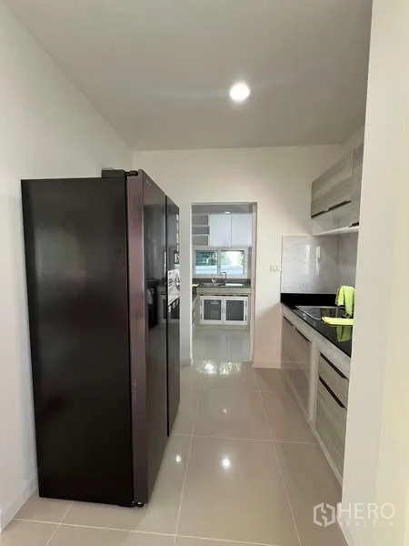 บ้าน ให้เช่าในBang Kapi, Bangkok - ครัวแบบแกลเลย์พร้อมตู้เย็นสีดำสูงและตู้บิลต์อิน เชื่อมต่อครัวไทย