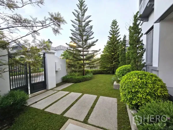 Detached House for rent in Saphan Sung, Bangkok - Private garden with stepping‑stone path, evergreens and a black metal gate.