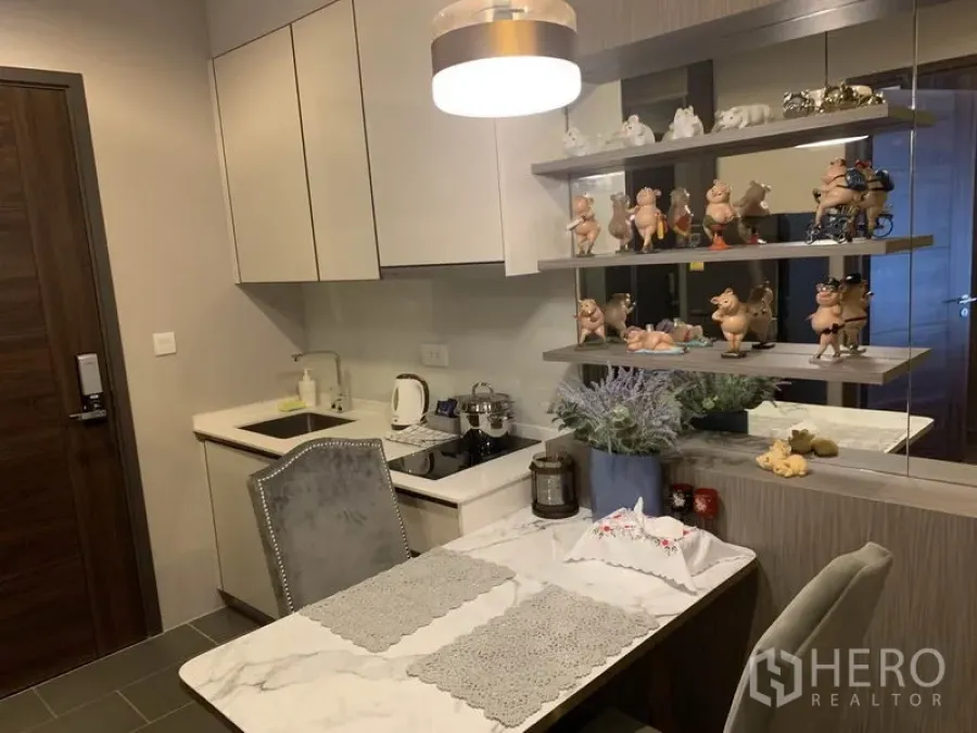 公寓 出售在Watthana, Bangkok - 吊灯下的温馨餐区，旁为配备电磁炉的现代小厨房与镜面置物架。