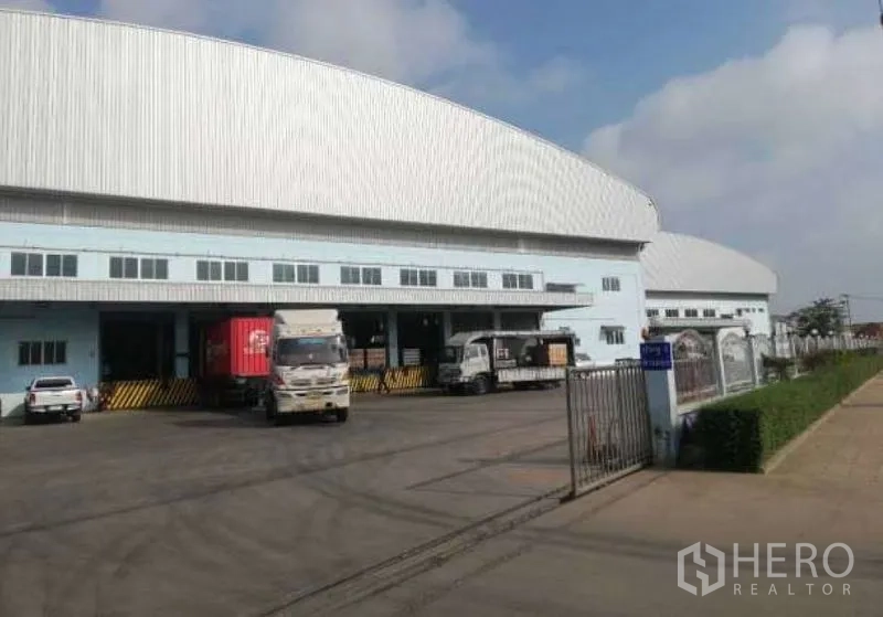 Warehouse for rent in Nong Chok, Bangkok - Large warehouse exterior with multiple dock-high loading bays, trucks, and a gated entry in Nong Chok, Bangkok.