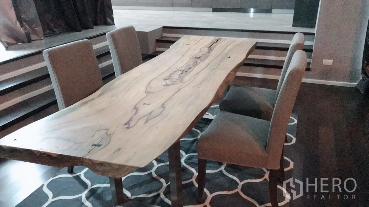 Condominium for rent or sale in Huai Khwang, Bangkok - Dining area with a live-edge wooden table and upholstered chairs over a geometric rug.