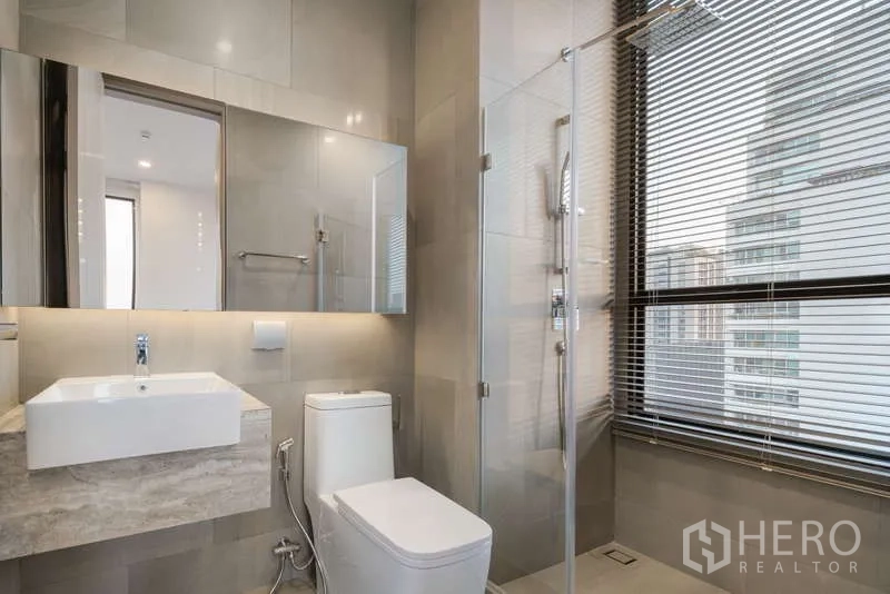 Condominium for rent - Modern bathroom with glass shower, floating vanity, toilet and large window with blinds.