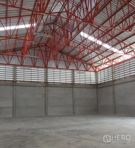 Warehouse for rent in Khlong Sam Wa, Bangkok - Open warehouse space beneath a metal roof with red truss framing and upper louver windows for airflow.