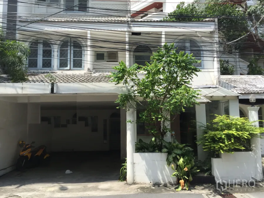 零售空间 出租在Watthana, Bangkok - 面向街道的白色低层建筑，拱形窗、带顶车位与绿植花坛，适合零售，靠近BTS通罗站。