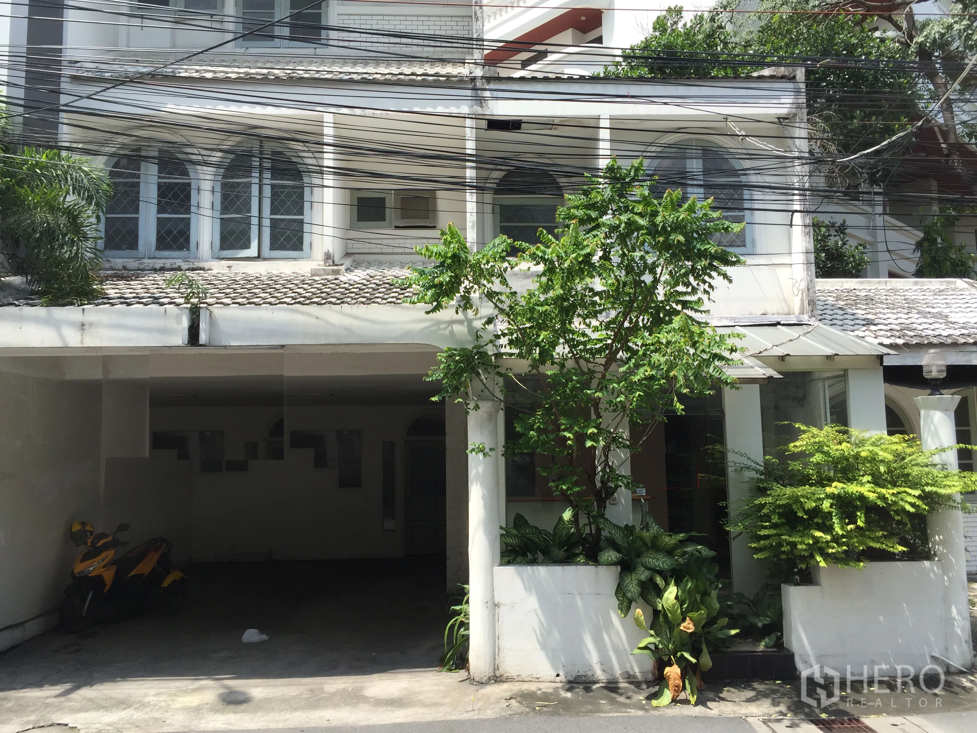 零售空间 出租在Watthana, Bangkok - 面向街道的白色低层建筑，拱形窗、带顶车位与绿植花坛，适合零售，靠近BTS通罗站。