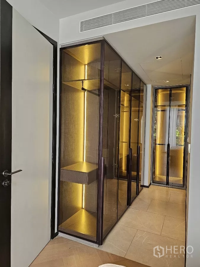 公寓 出租在Watthana, Bangkok - 走廊两侧玻璃衣柜，内嵌暖色灯光。