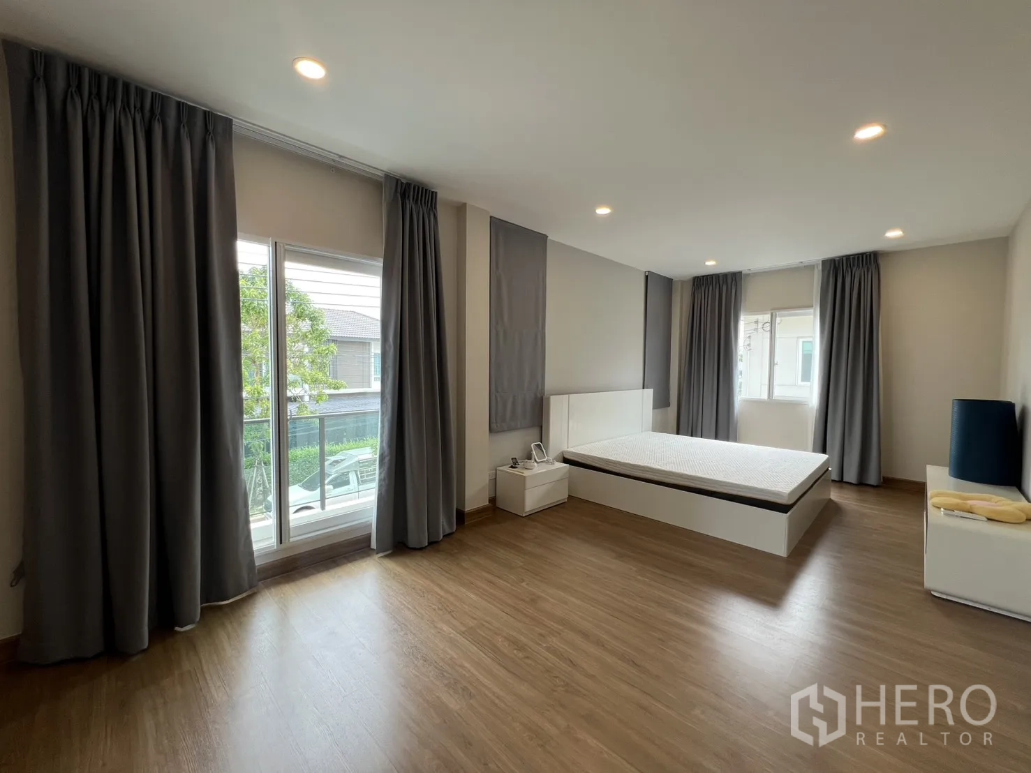 Detached House for rent in Lat Krabang, Bangkok - Spacious master bedroom with large windows, platform bed, wood floors, and curtains.