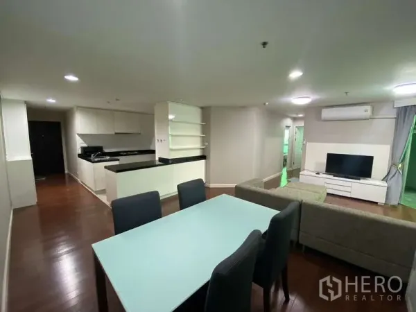 Condominium for  in Huai Khwang, Bangkok - Dining area with frosted‑glass table and four chairs beside the living room and TV.