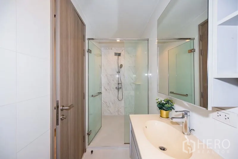 公寓 出租在Watthana, Bangkok - 紧凑浴室，玻璃淋浴间与长镜盥洗台。