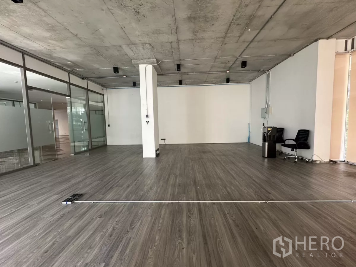 零售空间 出租 - 室内深景，木纹地板、白色墙面、外露管线，与通向走道的玻璃墙。