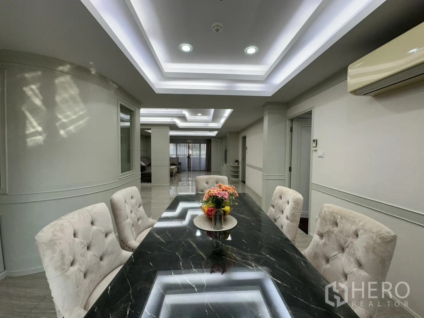 Condominium for rent in Watthana, Bangkok - Elegant dining room with a black marble table, tufted chairs, and cove lighting.