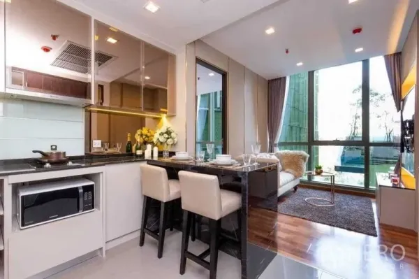 Condominium for sale in Ratchathewi, Bangkok - Open-plan kitchen with dining counter flowing to a bright living area with large windows and wood floors.