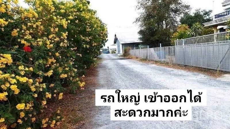 货栈 出租在Nakhon Pathom - 宽阔的碎石路，旁有开花灌木和金属围栏，适合卡车通行至仓库。