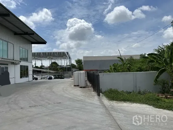 货栈 出租在Lat Krabang, Bangkok - 办公室旁宽阔混凝土车道通往仓库，围墙与绿化清晰可见。