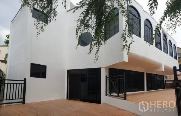 带办公室的家 出租或出售在Bang Na, Bangkok - 侧面角度，白色外墙、拱形窗与宽阔木质露台。