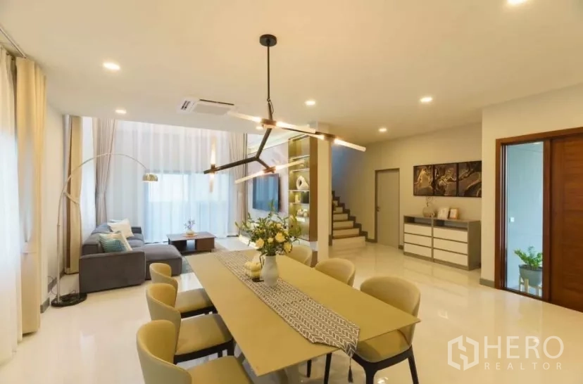 Detached House for rent or sale in Bang Phli, Samut Prakan - Open-plan living and dining area with long table, designer chandelier, bright windows and staircase.