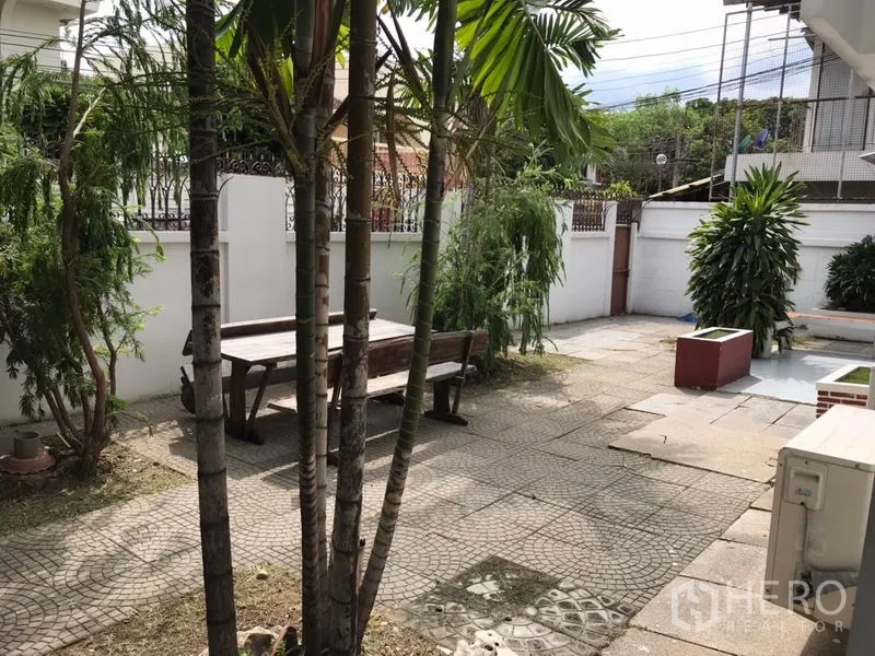 บ้าน ให้เช่าในPhra Khanong, Bangkok - ลานหน้าบ้านปูกระเบื้องพร้อมม้านั่งไม้ รายล้อมด้วยต้นไม้และกำแพงสีขาว