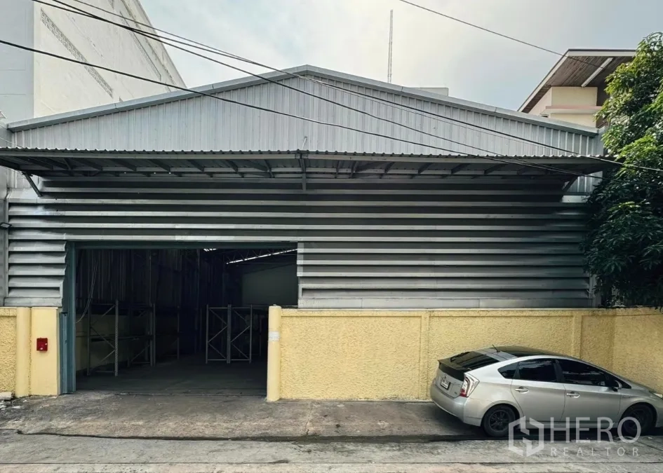 Warehouse for rent in Din Daeng, Bangkok - Street view of a metal-clad warehouse in Huai Khwang with a wide loading entrance and yellow boundary wall.
