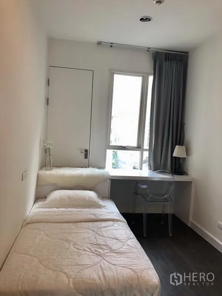คอนโด ให้เช่าในPathum Wan, Bangkok - ห้องนอนเล็กอบอุ่น เตียงเดี่ยว โต๊ะทำงานริมหน้าต่าง และผ้าม่านสีเทา