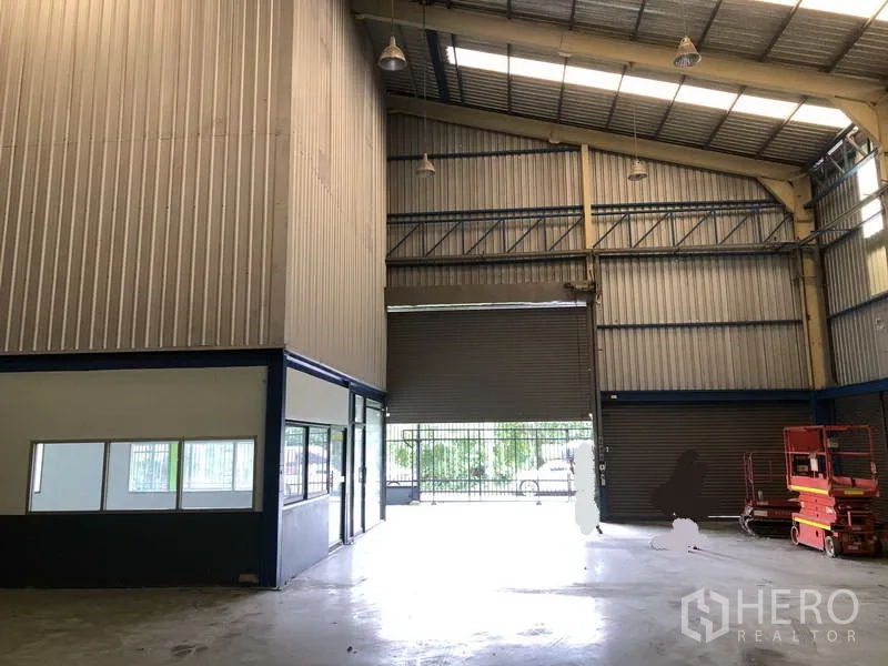 Warehouse for rent in Bang Phli, Samut Prakan - Spacious hall with high roller door, roof lights, and equipment space at the rear.