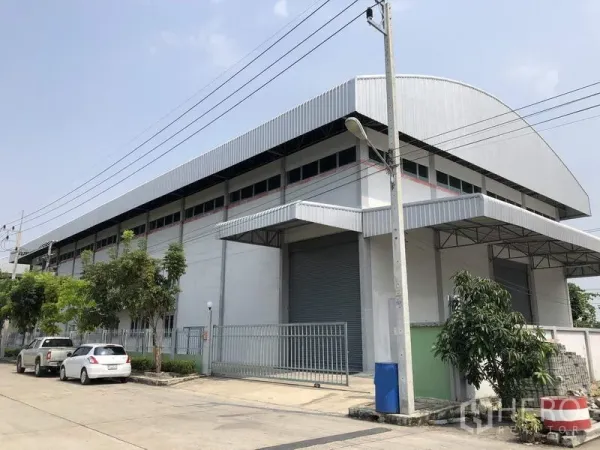 工厂 出租在Lam Luk Ka, Pathum Thani - Lam Luk Ka 现代灰色工厂外观，弧形金属屋顶、卷闸门与大门入口。
