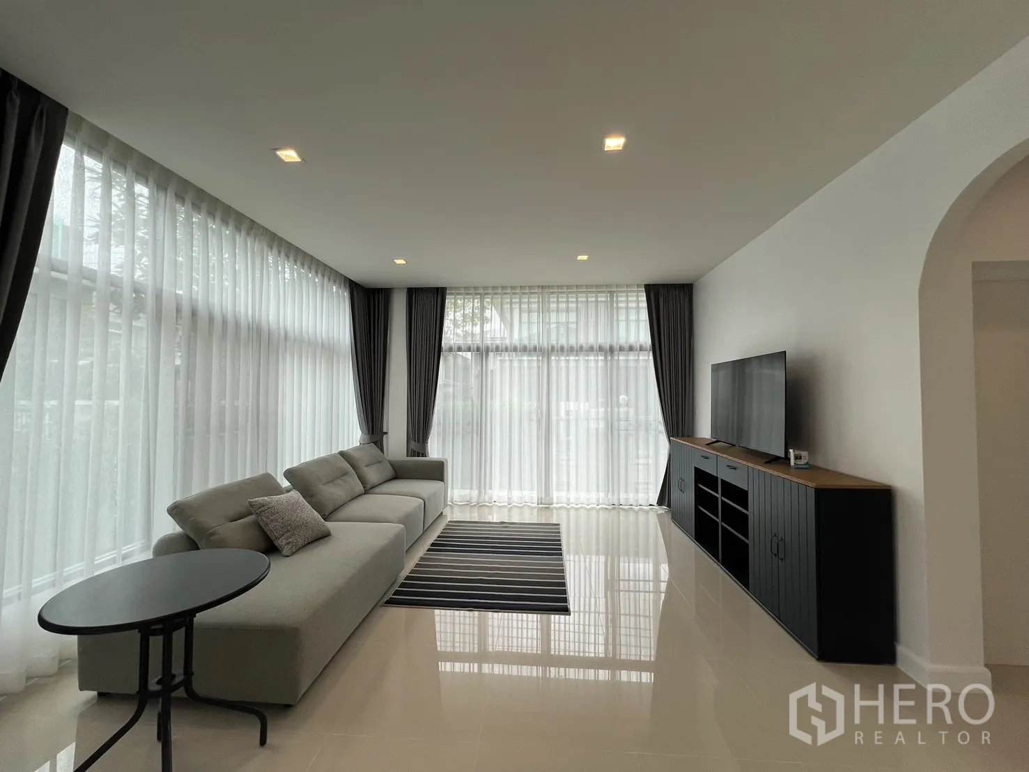 独立式住宅 出租在Bang Kapi, Bangkok - 采光充足的客厅，灰色转角沙发、电视柜与纱帘。