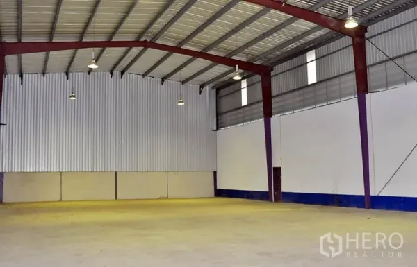 Warehouse for rent in Pathum Thani - Spacious warehouse interior with high steel roof, hanging high-bay lights, ventilation panels, and smooth concrete floor.