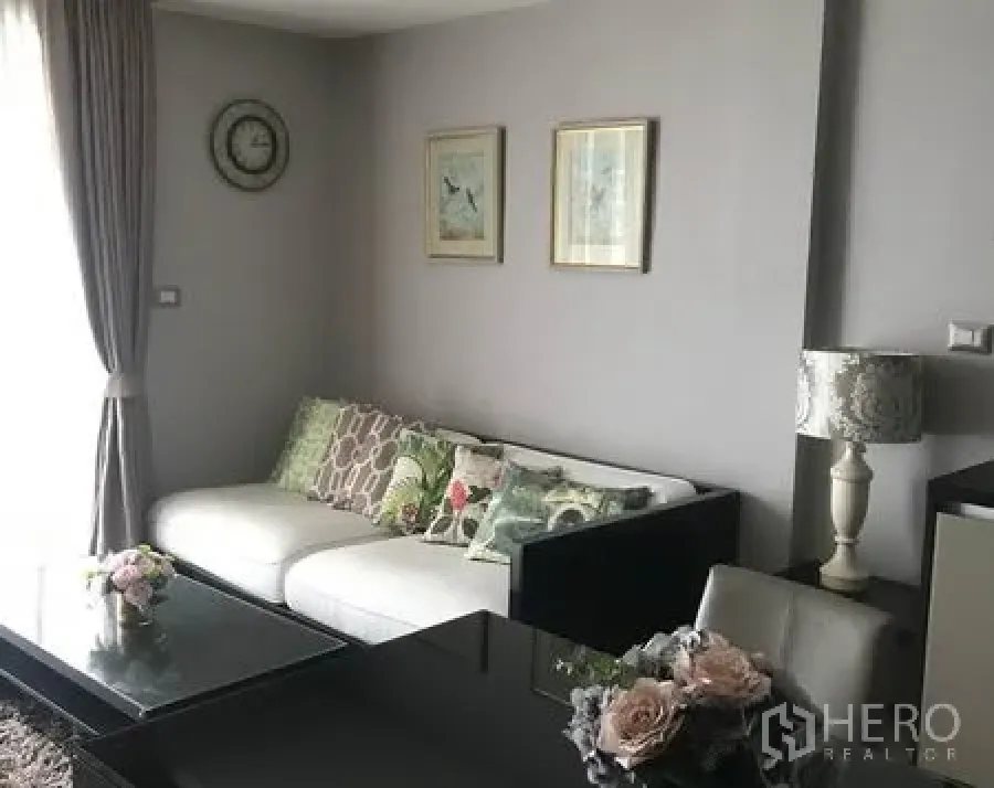 Condominium for rent in Watthana, Bangkok - Bright living area with white sofa, glass coffee table, curtains and wall art in a modern Ekkamai condo.