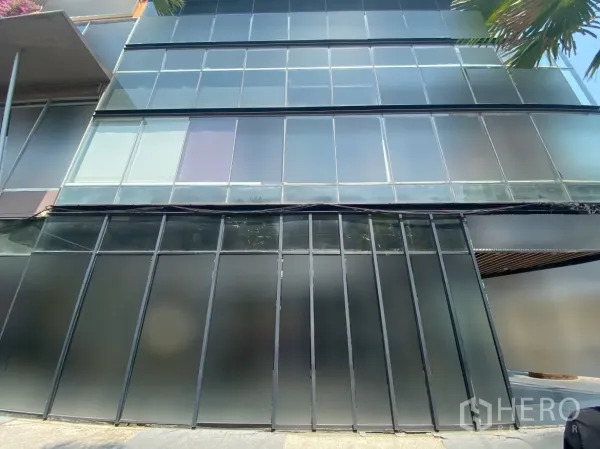 零售空间 出租在Watthana, Bangkok - 多层玻璃幕墙特写，下部磨砂面板与店前人行道。