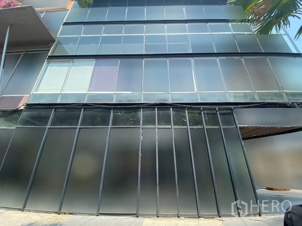 零售空间 出租在Watthana, Bangkok - 多层玻璃幕墙特写，下部磨砂面板与店前人行道。