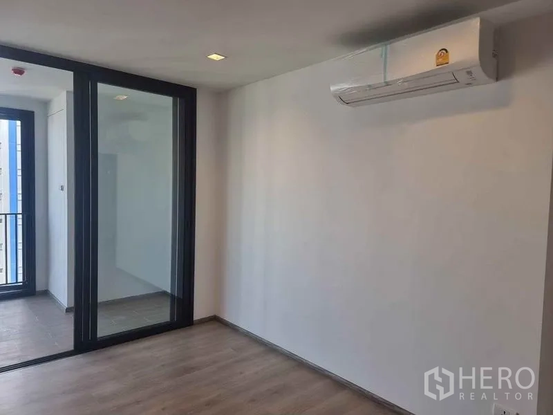 Condominium for sale in Phaya Thai, Bangkok - Living area with wood flooring, air conditioner and glass partition to the balcony.