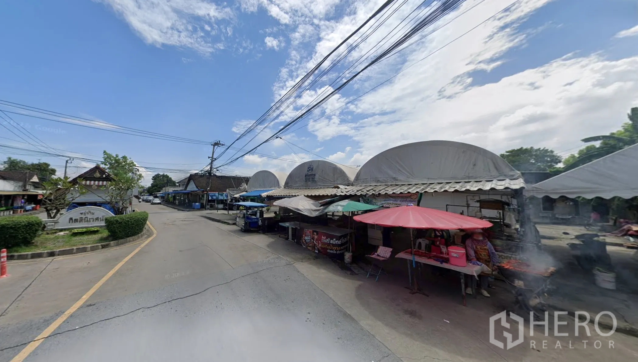 Land for sale in Bang Kapi, Bangkok - Row of vendor stalls with canopies along a curved neighborhood road.