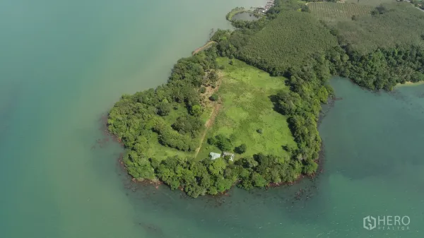 Land for sale in Khlong Toei, Bangkok - Aerial view of a lush green peninsula surrounded by turquoise water with a rocky shoreline.