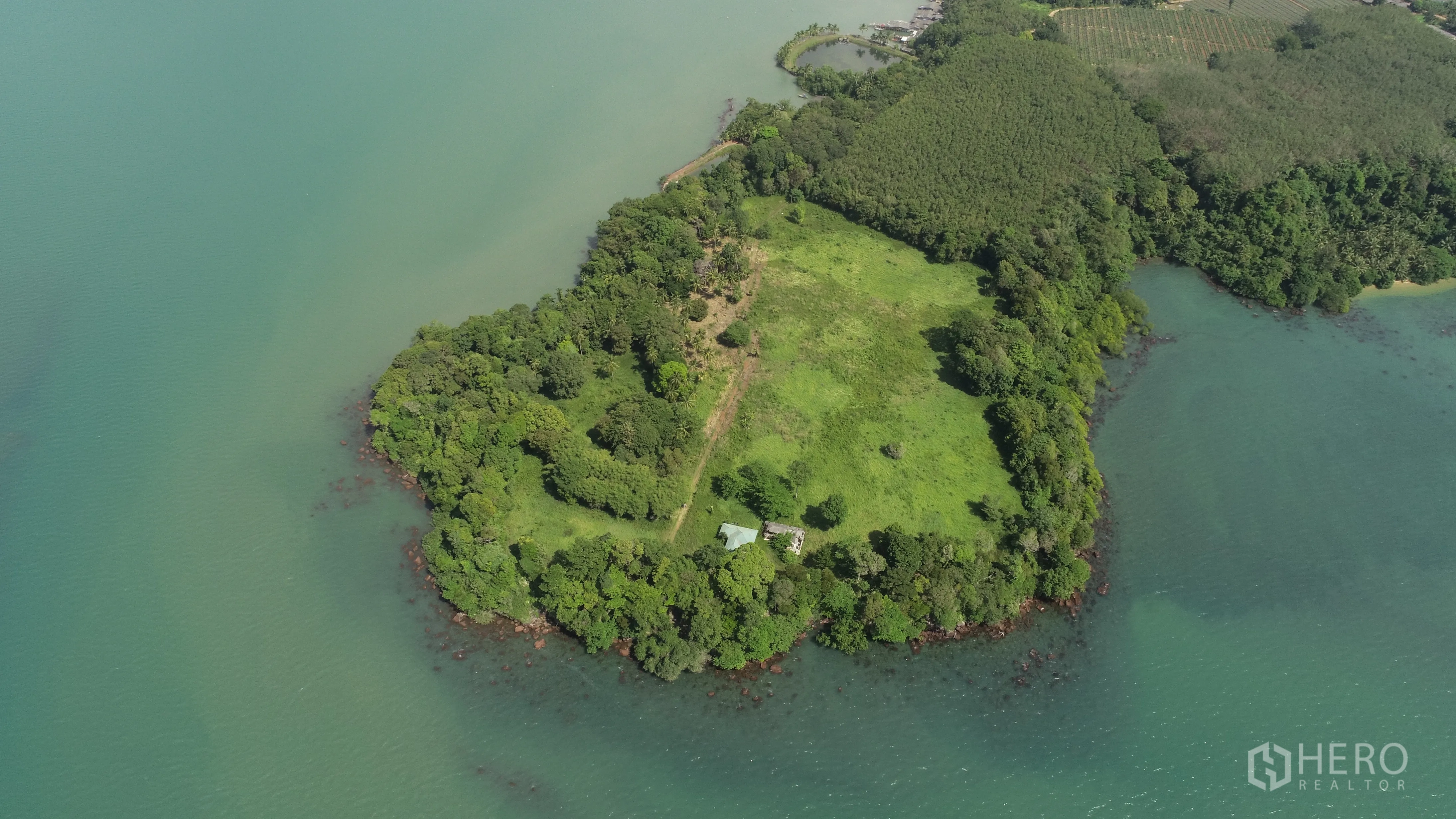 Land for sale in Khlong Toei, Bangkok - Aerial view of a lush green peninsula surrounded by turquoise water with a rocky shoreline.