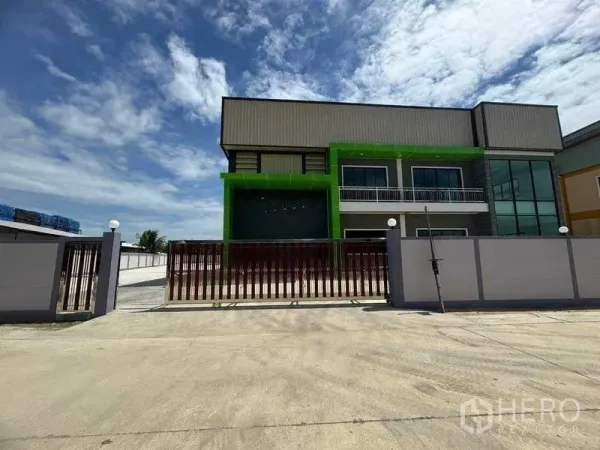 Factory for sale in Samut Sakhon - Front elevation of factory behind sliding gate with secure perimeter wall and driveway.