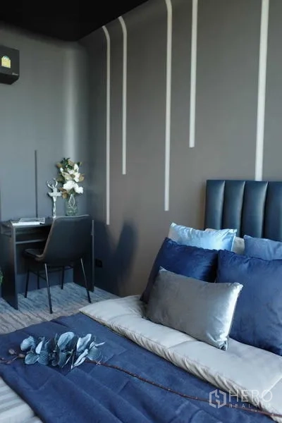 คอนโด ขาย - ห้องนอนอบอุ่นพร้อมโต๊ะทำงาน ผนังสีเทาและเส้นไฟแนวตั้ง