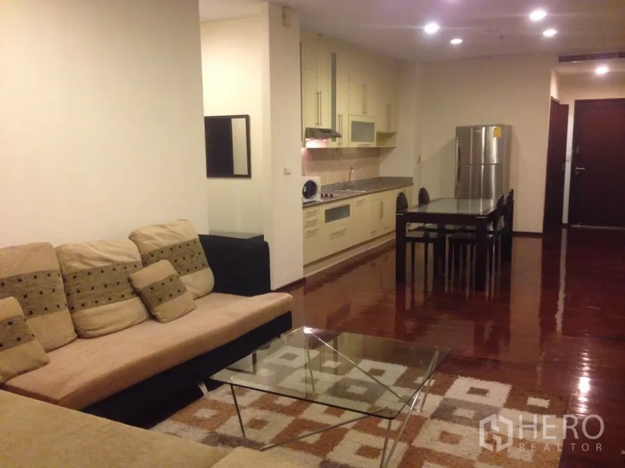 คอนโด ให้เช่าในWatthana, Bangkok - พื้นที่นั่งเล่นแบบโอเพ่นในคอนโดทองหล่อ โซฟาเบจ โต๊ะกลางกระจก ชุดทานอาหาร และครัวบิลท์อินพร้อมตู้เย็น พื้นไม้เงางาม