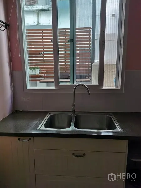 联排别墅 出租在Wang Thonglang, Bangkok - 厨房窗户上方为不锈钢双槽水槽与深色台面。
