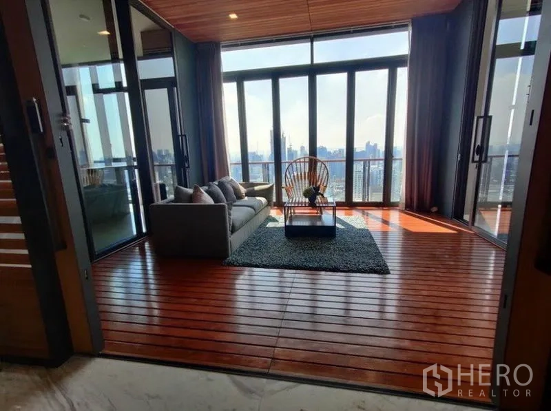 Condominium for rent in Watthana, Bangkok - Enclosed sunroom with wooden deck flooring, sofa and lounge chair, framed by tall glass doors with city views.