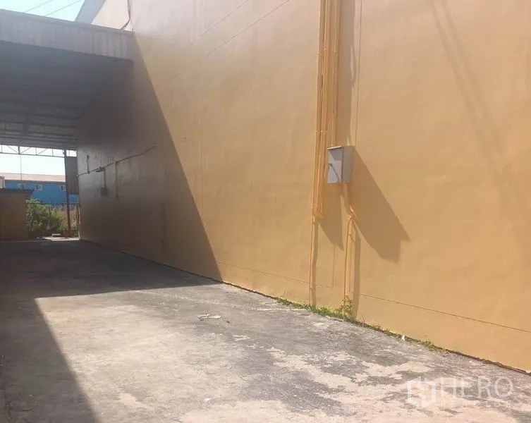 คลังสินค้า ให้เช่าในPathum Thani - ทางเดินภายนอกยาว พื้นคอนกรีต ข้างกำแพงสีเหลืองและหลังคาคลุมสำหรับโหลดสินค้า.