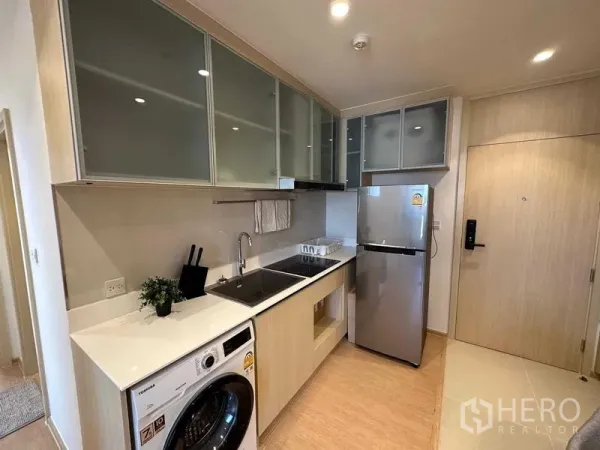 公寓 出售 - 现代一字型厨房，吊柜、灶台、水槽、冰箱与洗衣机。