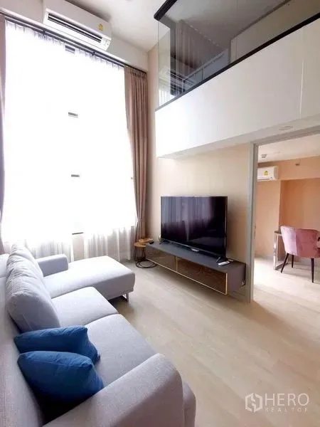 Condominium for rent in Sathon, Bangkok - Cozy living room with TV, sectional sofa, high window, and an adjacent workspace.