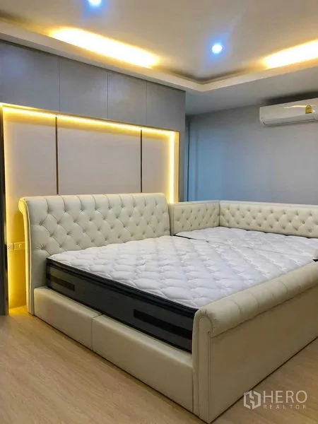 Home Office for rent or sale in Pak Kret, Nonthaburi - Bedroom with tufted L-shaped bed, soft ceiling lighting and built-in headboard.