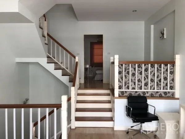 联排别墅 出租在Prawet, Bangkok - 半层挑高走廊，木楼梯、白色栏杆与办公椅。