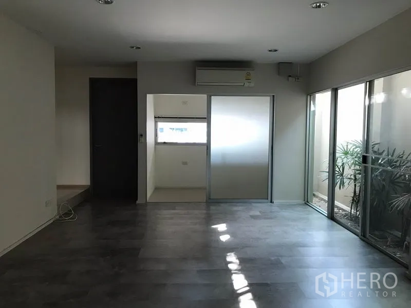 ทาวน์เฮาส์ ให้เช่าในSuan Luang, Bangkok - ห้องนั่งเล่นสว่าง พื้นไม้สีเข้ม แอร์ และประตูกระจกบานเลื่อนไปยังห้องเอนกประสงค์และคอร์ทยาร์ด