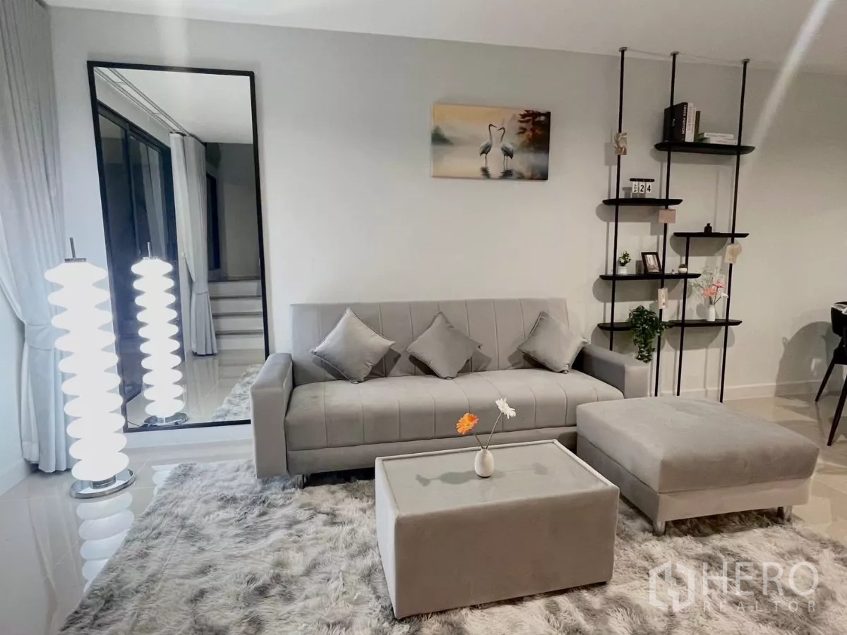 ทาวน์เฮาส์ ให้เช่าในSamut Prakan - มุมนั่งเล่นโซฟาสีเทา ออตโตมัน พรมขนฟู และโคมไฟตั้งพื้น