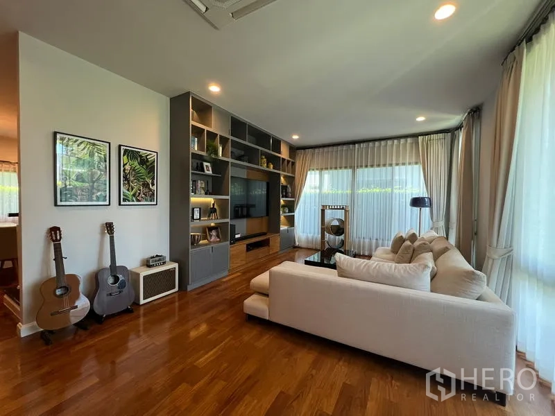 Detached House for rent in Bang Kapi, Bangkok - Living room with L-shaped sofa, built-in media wall and display shelving, guitars on stand.