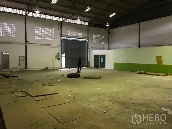 Warehouse for rent in Bang Phli, Samut Prakan - Empty warehouse interior showing large steel loading door, ventilation blocks, high ceiling and durable concrete flooring.