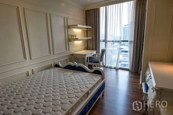 Condominium for rent in Watthana, Bangkok - Bright bedroom with bed, built-in desk and shelves beside floor-to-ceiling windows overlooking the city.